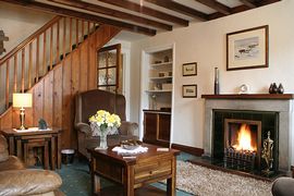 Cosy lounge with beamed ceiling, open fireplace and decorative stone alcoves.